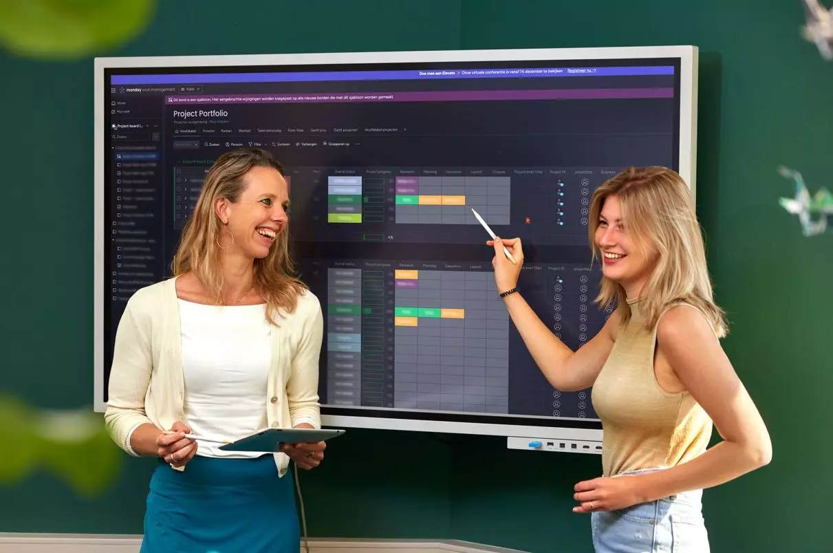 Een jonge medwerker in een winkel staat achter een tafel en vouwt denim broeken. Ze heeft een glimlach op haar gezicht.