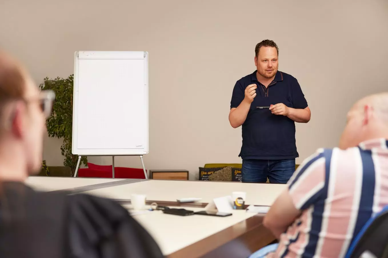 Een acteur op een stoel wacht terwijl een cameraman en iemand van productie aan het praten zijn.